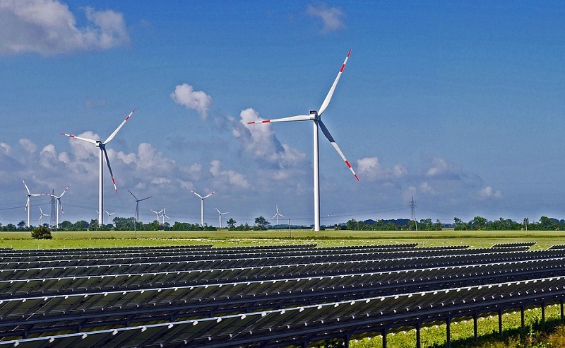 Windräder vor blauem Himmel, im Vordergrund Solaranlagen auf einem Feld